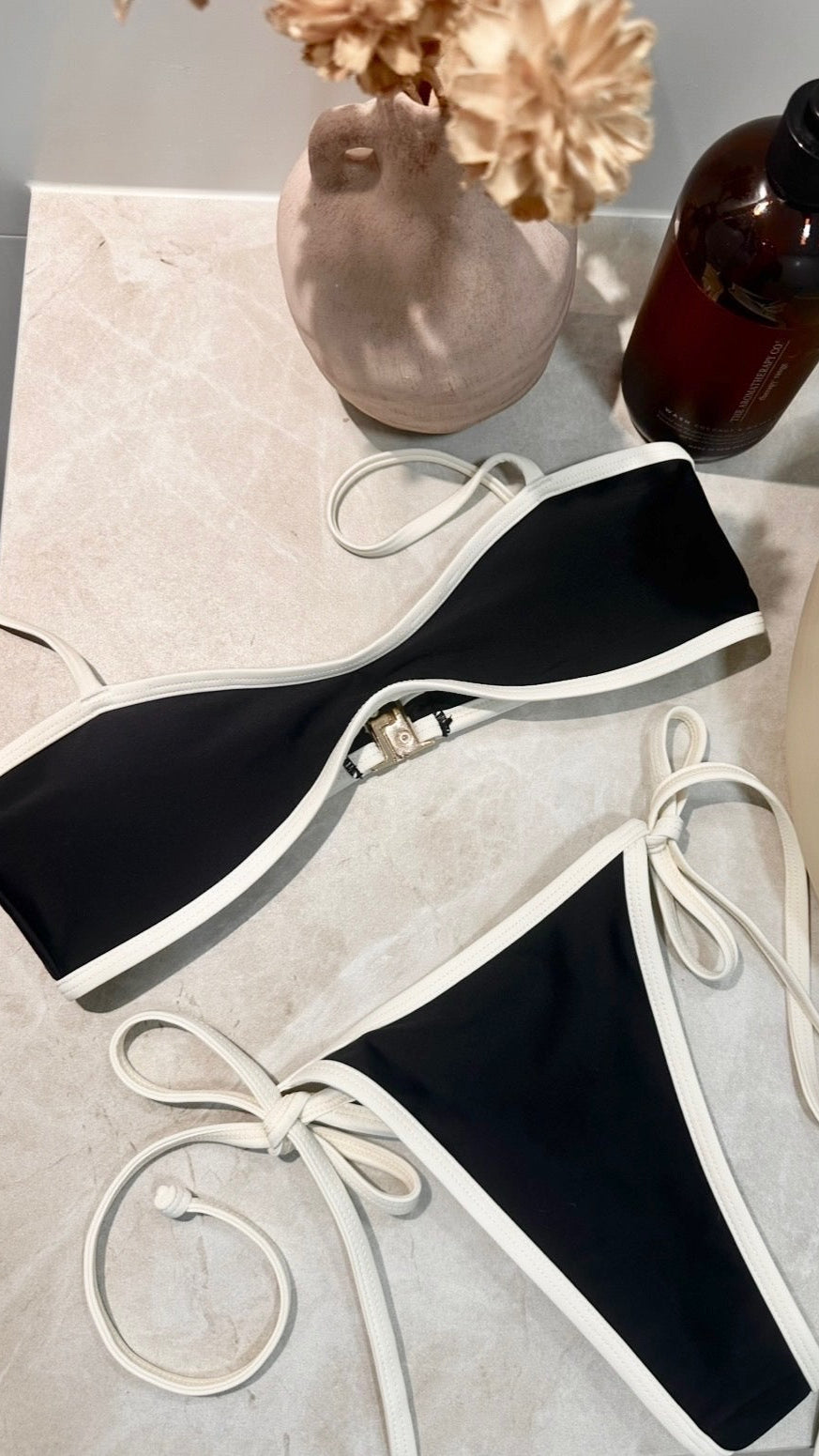 Black bikini set on a marble surface with a vase and bottle in the background