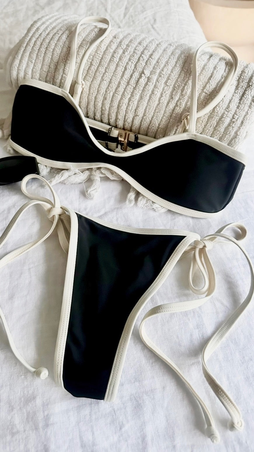 Black and white bikini set on a white surface with sunglasses.