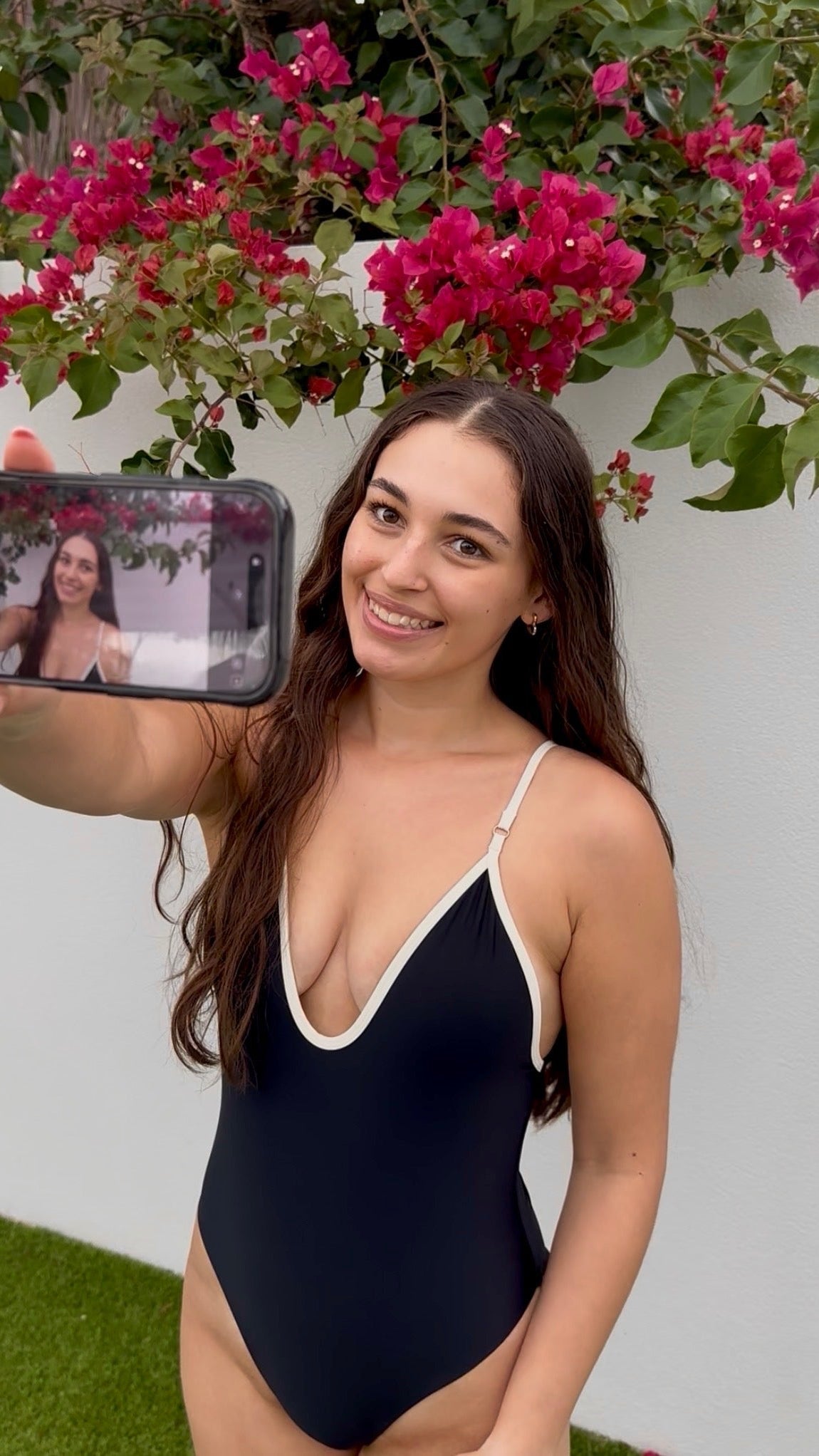 Woman taking a selfie in a black swimsuit with pink flowers in the background